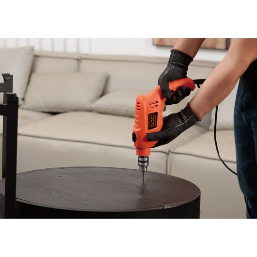 BLACKDECKER TB555 orange corded electric drill used on a round dark wood table in a living room.