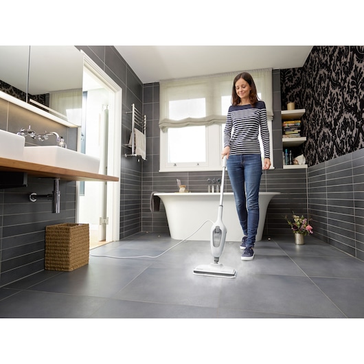 BLACKDECKER VL1300 steam mop being used on gray tile bathroom floor, bathtub and sink in background.