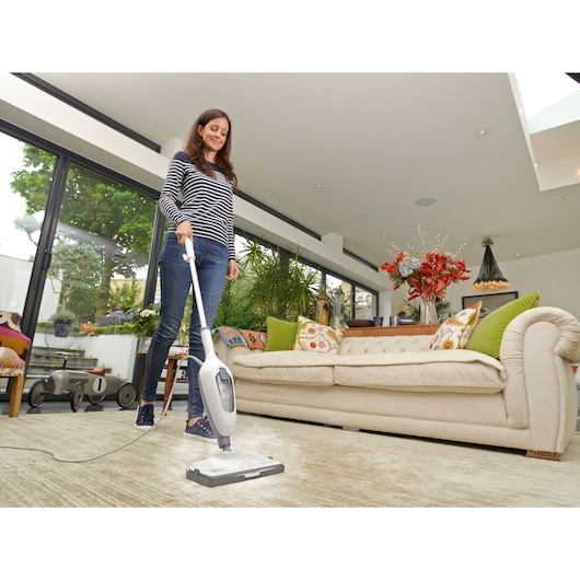 Photo of BLACKDECKER VL1300 steam mop cleaning a light carpet in a modern living room with a beige sofa.